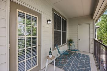 A small balcony with a blue chair and a table with a bottle on it.